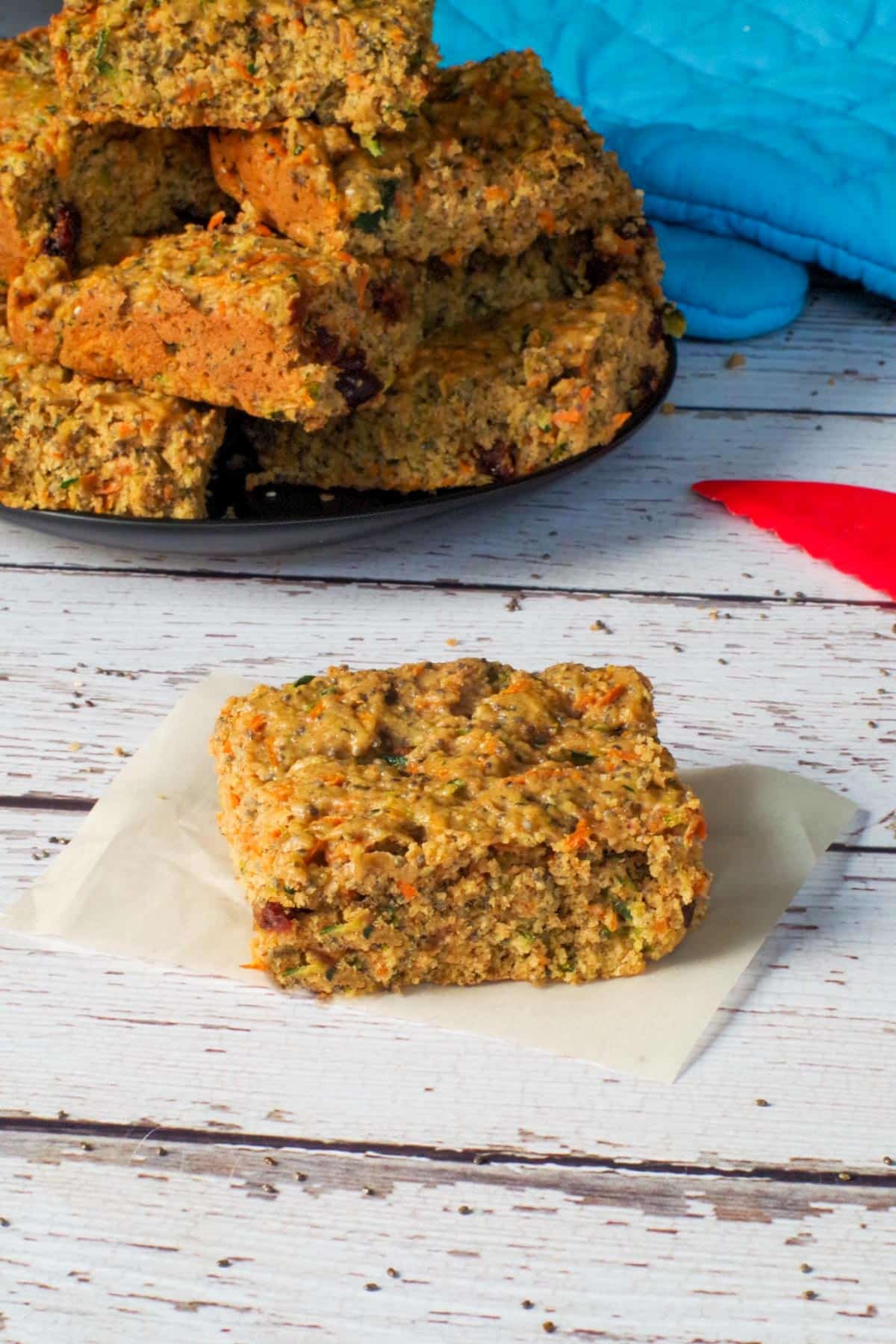 Zucchini bar on a piece of parchment paper with a plate of more zucchini bars in the background