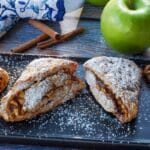 apple cinnamon scones on a black serving platter with a green apple and blue paisley patterned oven mitts in the background