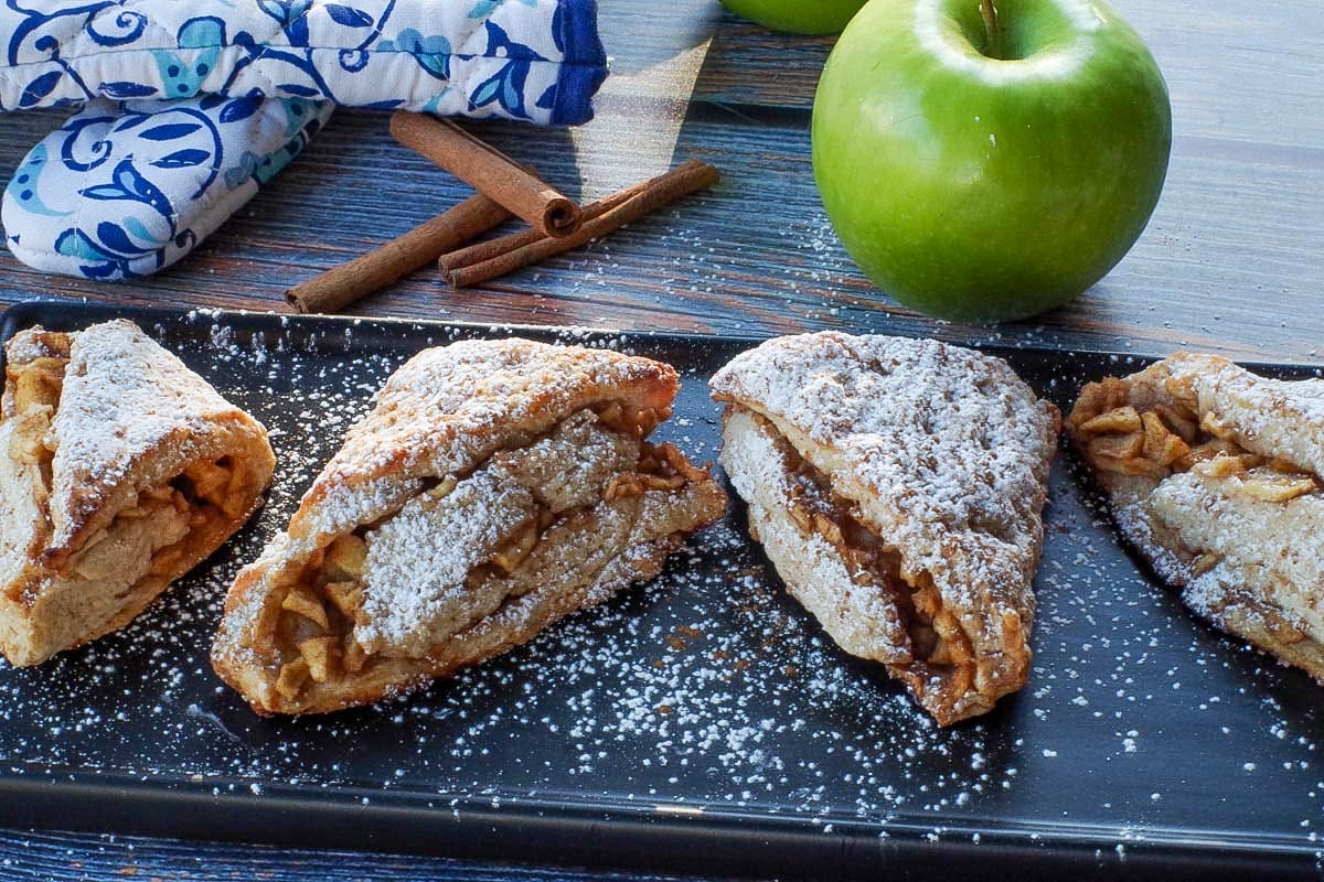 apple cinnamon scones on a black serving platter with a green apple and blue paisley patterned oven mitts in the background