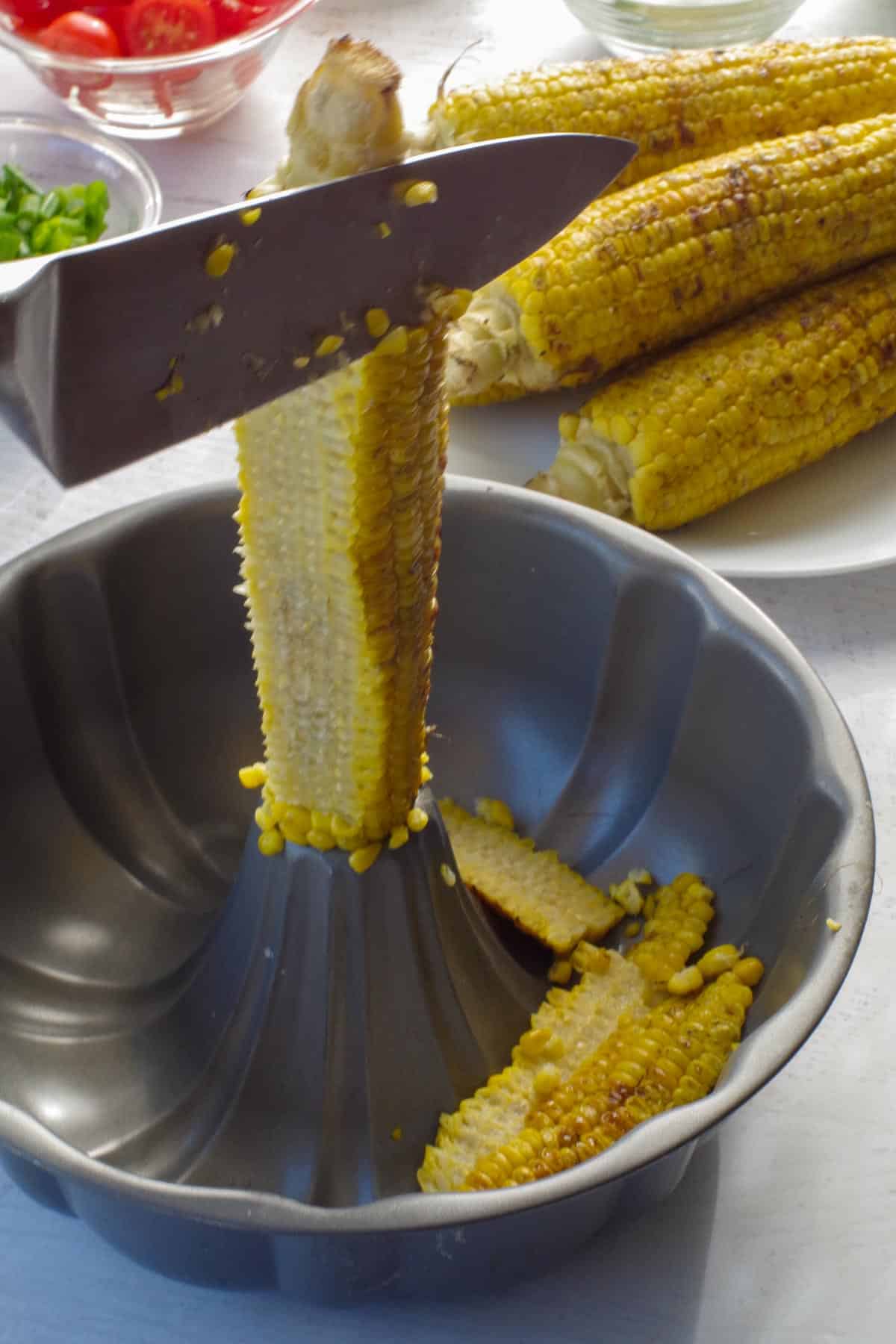 corn being cut off the cob with a knife using a bundt pan