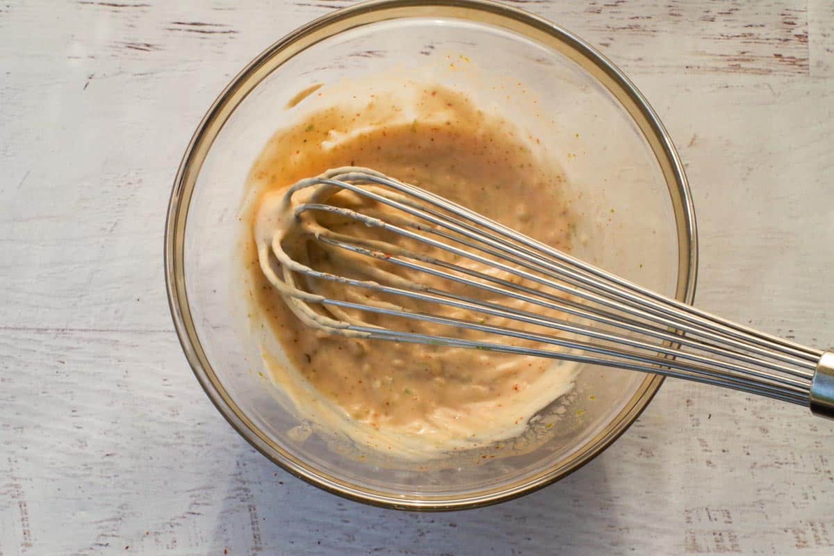 Mexican Street Corn pasta salad dressing in a glass bowl, being mixed with a whisk