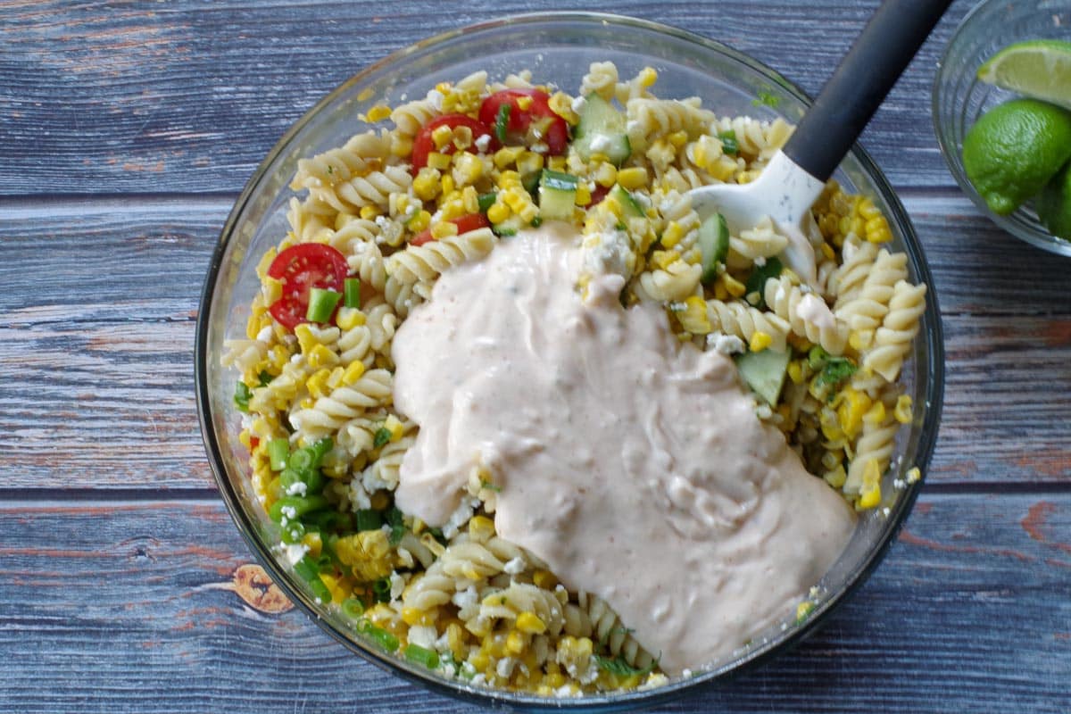 dressing on top of mixed together salad ingredients in a large glass bowl