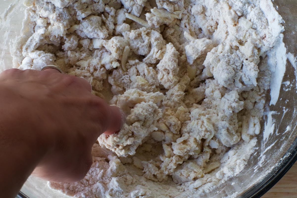 finger mixing cream into dry mixture in large glass bowl