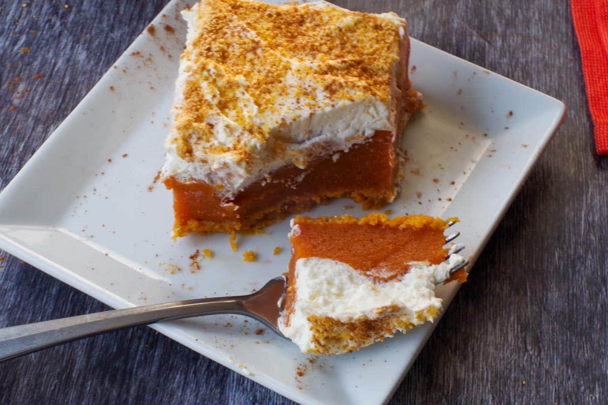 pumpkin layered dessert on a white plate, cut through with a fork and some dessert on the fork