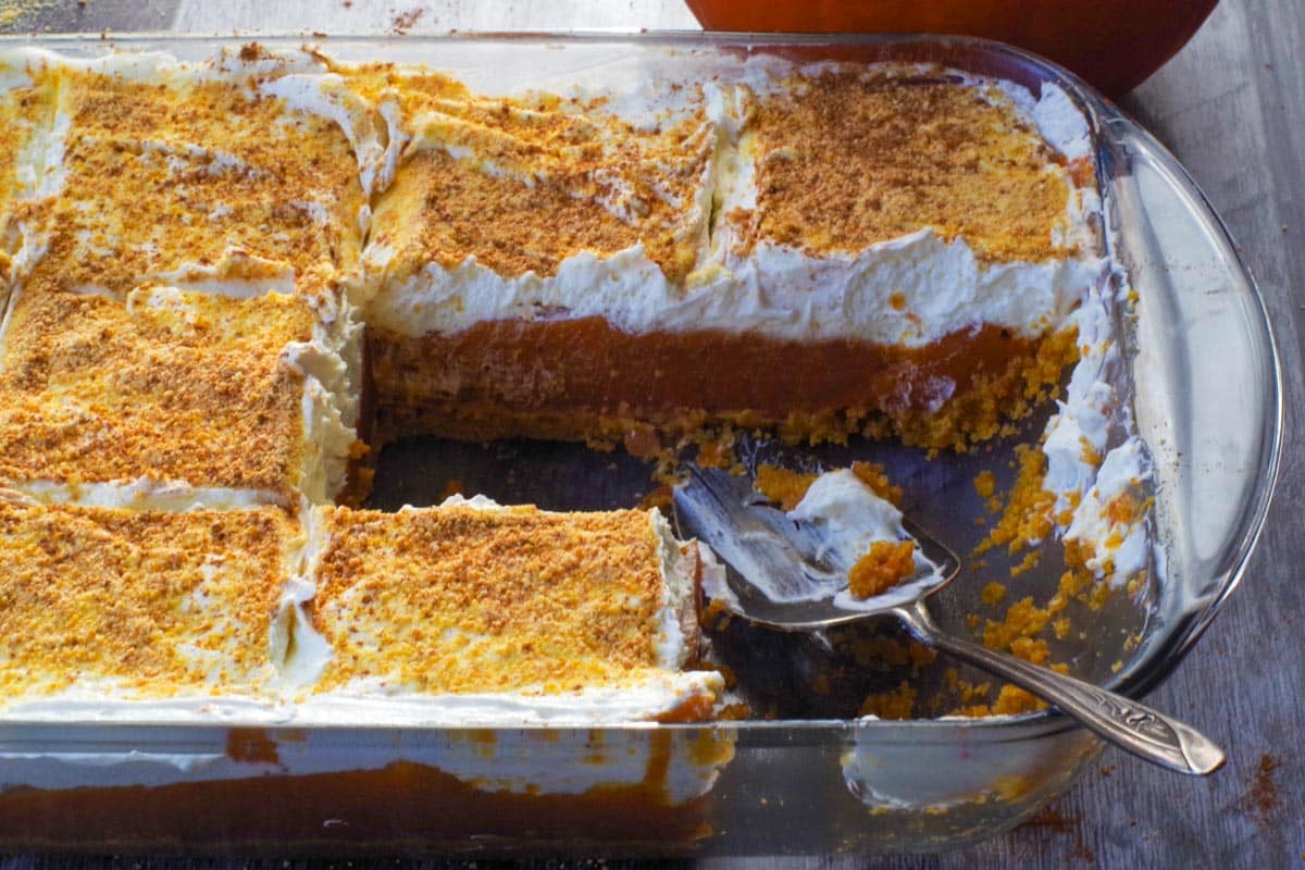 layered pumpkin dessert with pieces missing and pie lifter in the pan