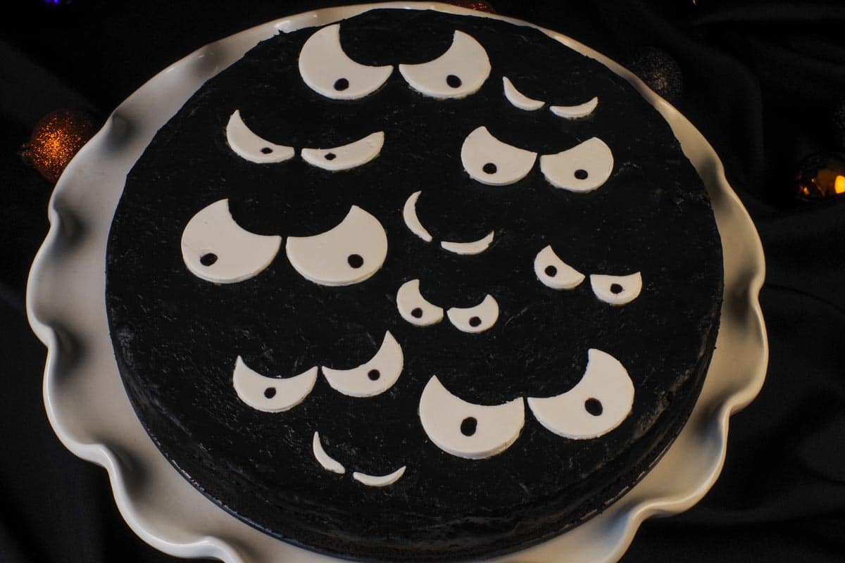 black cheesecake with white scary eyes on white cake stand