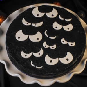 black cheesecake with white scary eyes on white cake stand