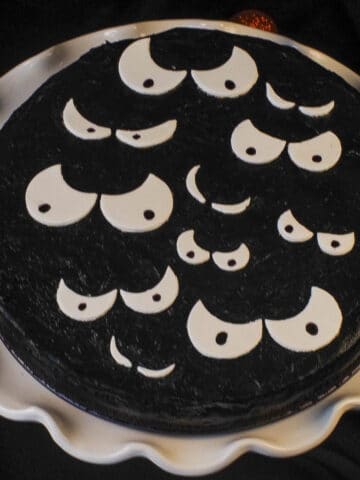 black cheesecake with white scary eyes on white cake stand