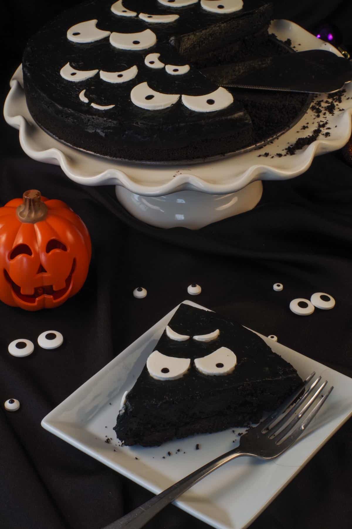 A slice of Halloween Party Cheesecake in front of a jack-o-lantern and a white cake stand with remaining cake in the background