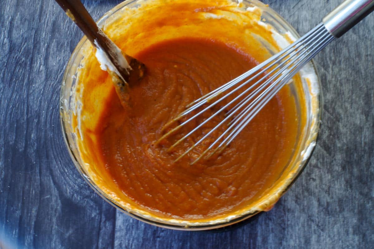 pumpkin mixture in glass bowl with whisk and wooden spoon