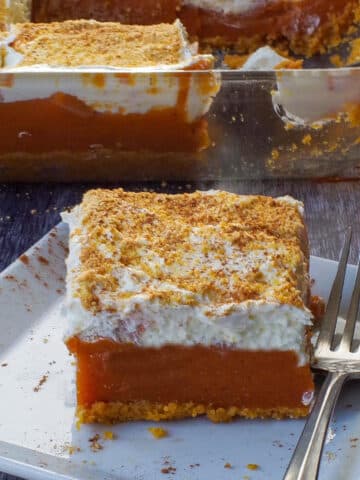 pumpkin layered dessert on a white plate with a fork and more in pan in background