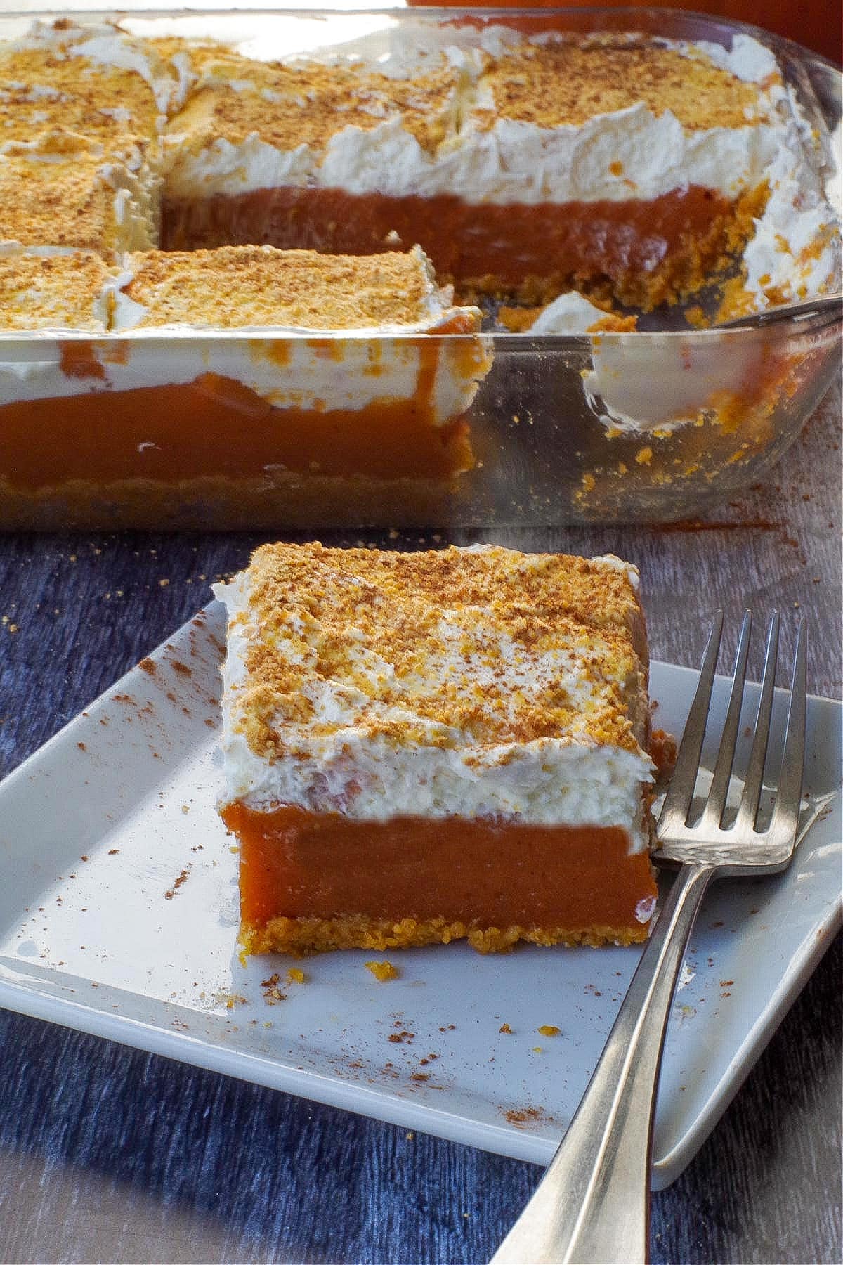 pumpkin layered dessert on a white plate with a fork and more in pan in background