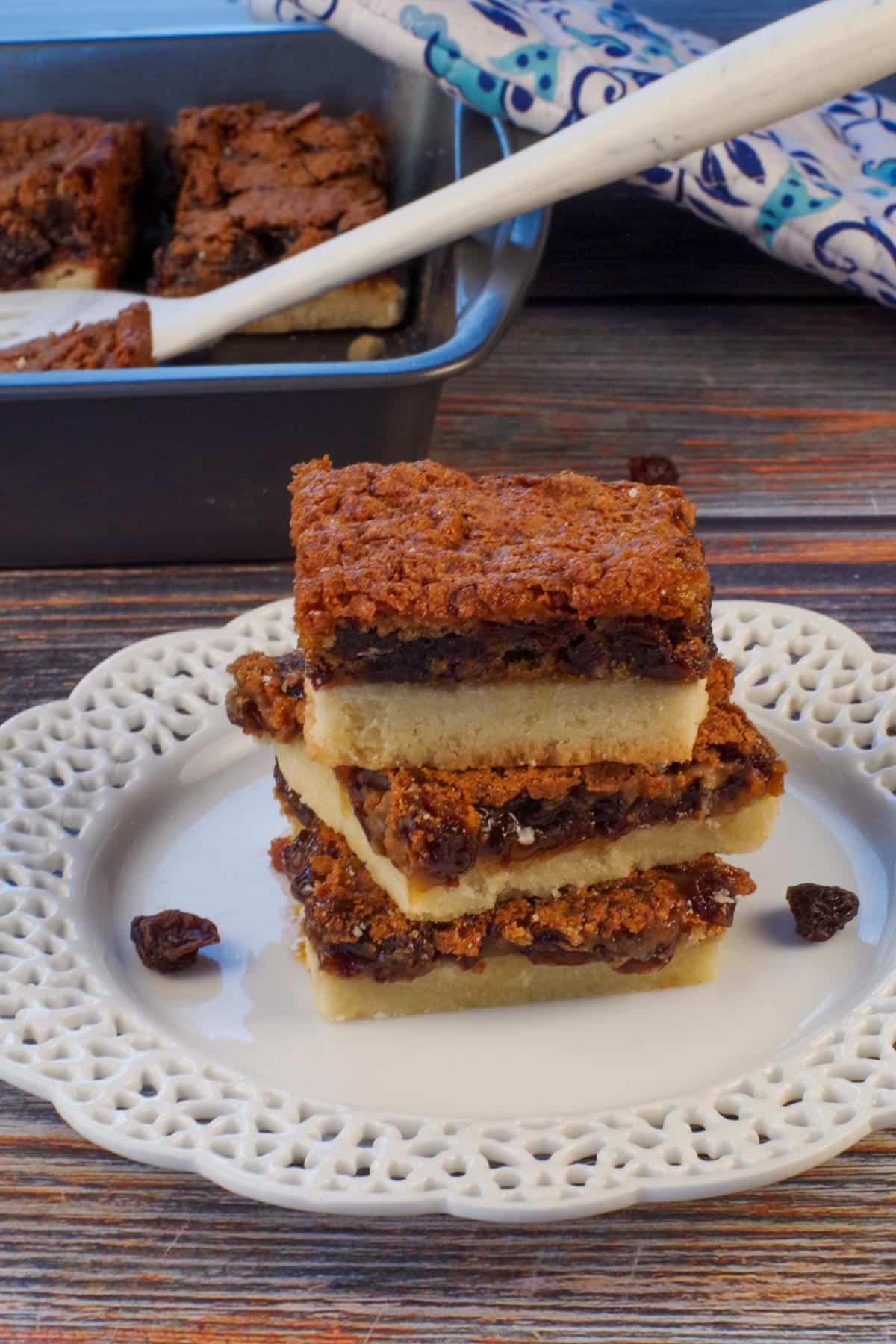 3 butter tart slices on a white plate with more in a pan in the background.