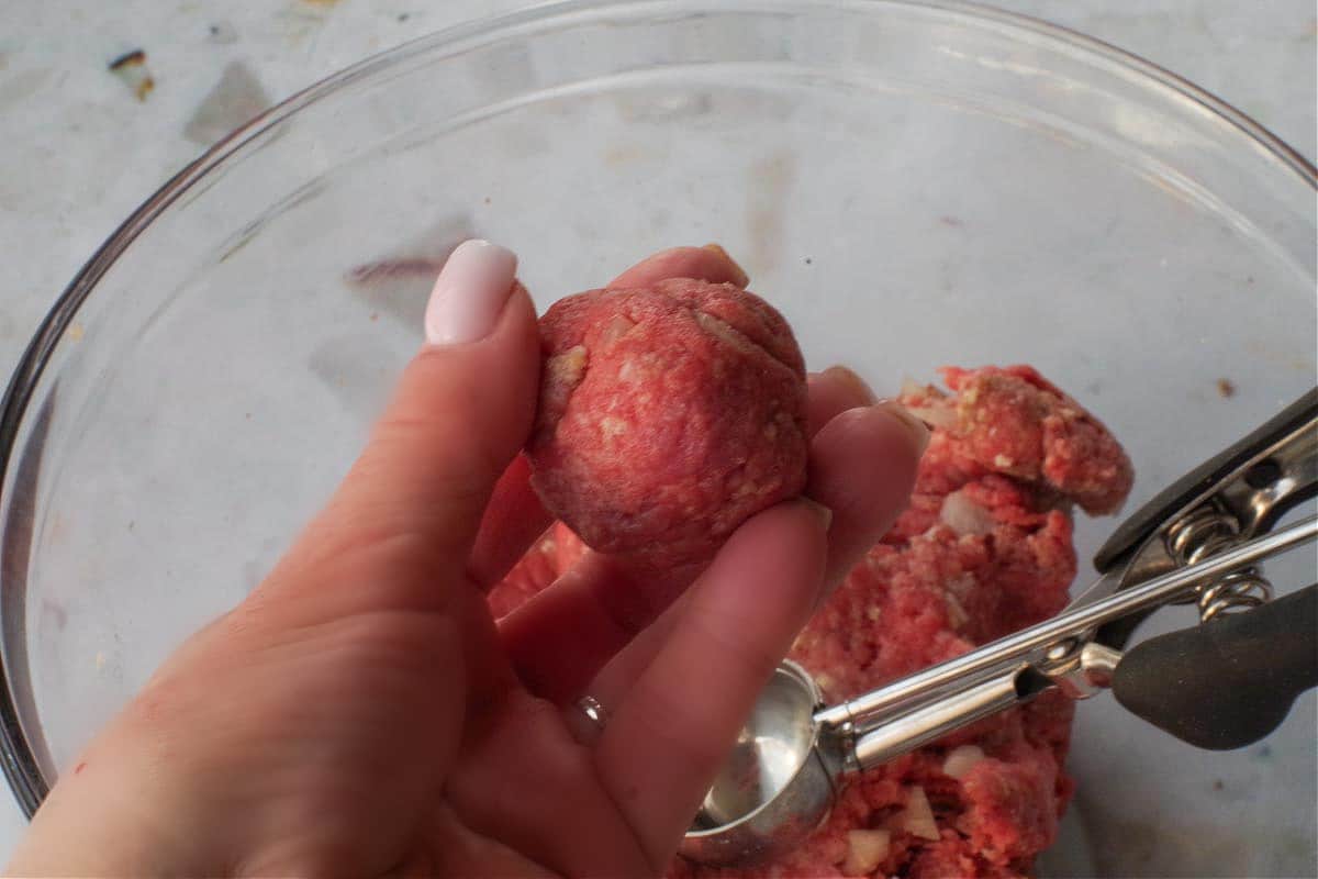 Formed meatball being held in hand over remaining meatball mixture