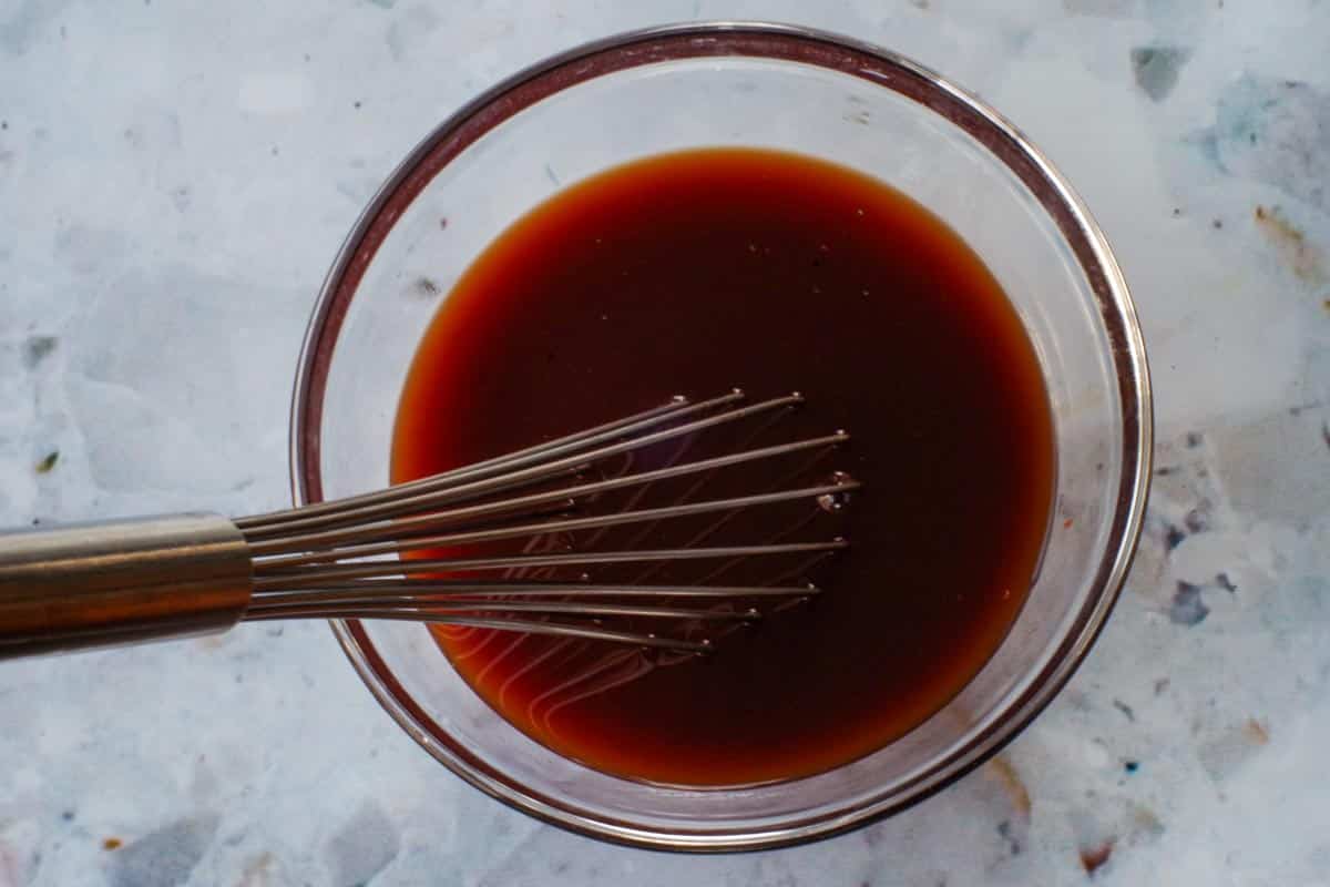 Sauce ingredients whisked together in glass bowl with metal whisk.