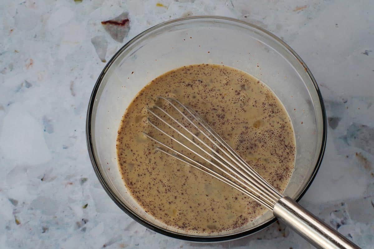 Liquid ingredients whisked together in large glass bowl with metal whisk.