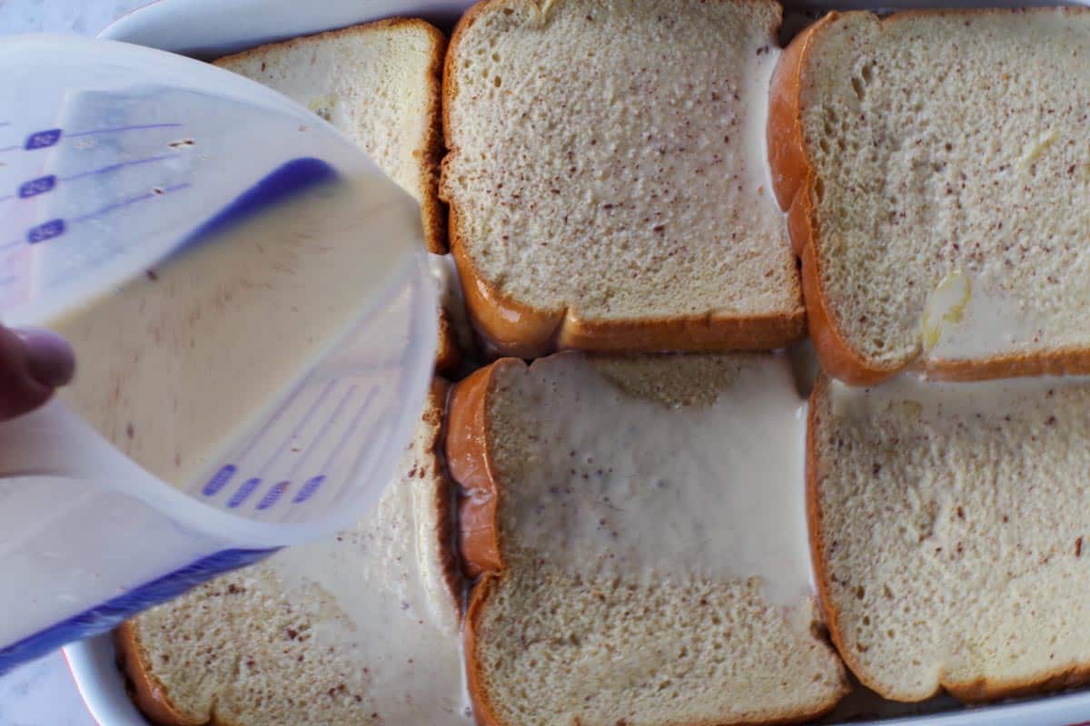 Liquid ingredients being poured over bread in casserole dish.