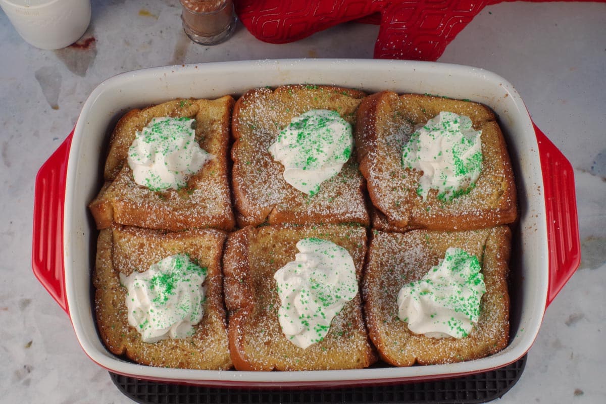 Baked Baileys French Toast Casserole garnished with whipped cream, cinnamon and powdered sugar.