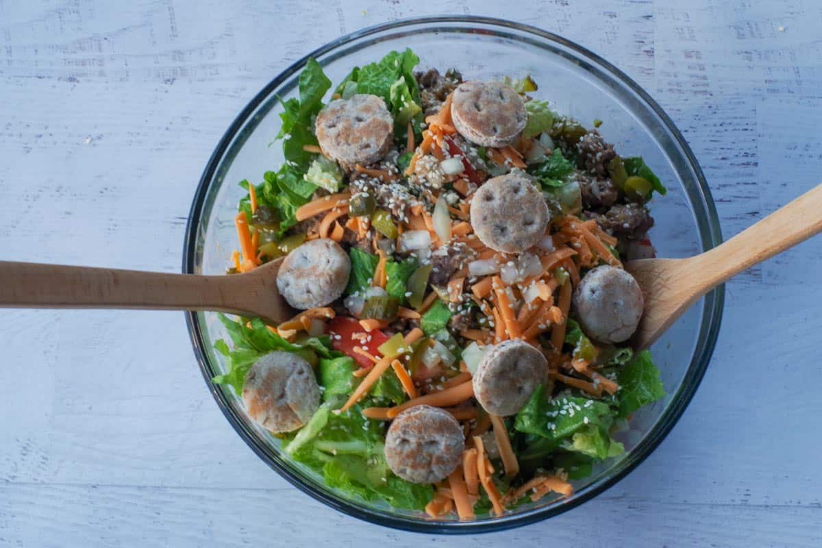 Big Mac salad in large glass bowl with wooden salad servers in bowl.