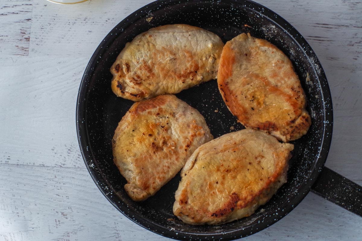 4 browned pork chops in frying pan.