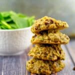 4 healthy chocolate spinach cookies stacked with a bowl of fresh spinach in the background.