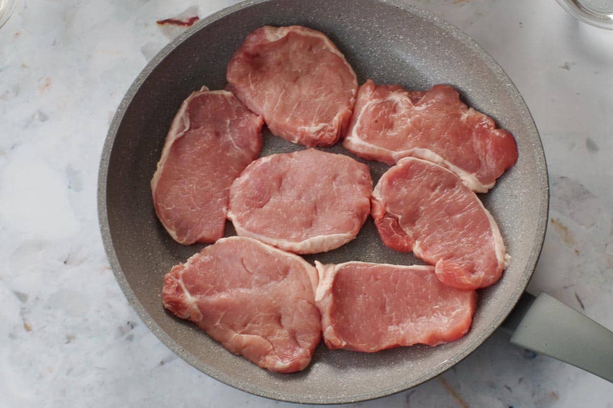 Raw pieces of boneless pork in a frying pan.
