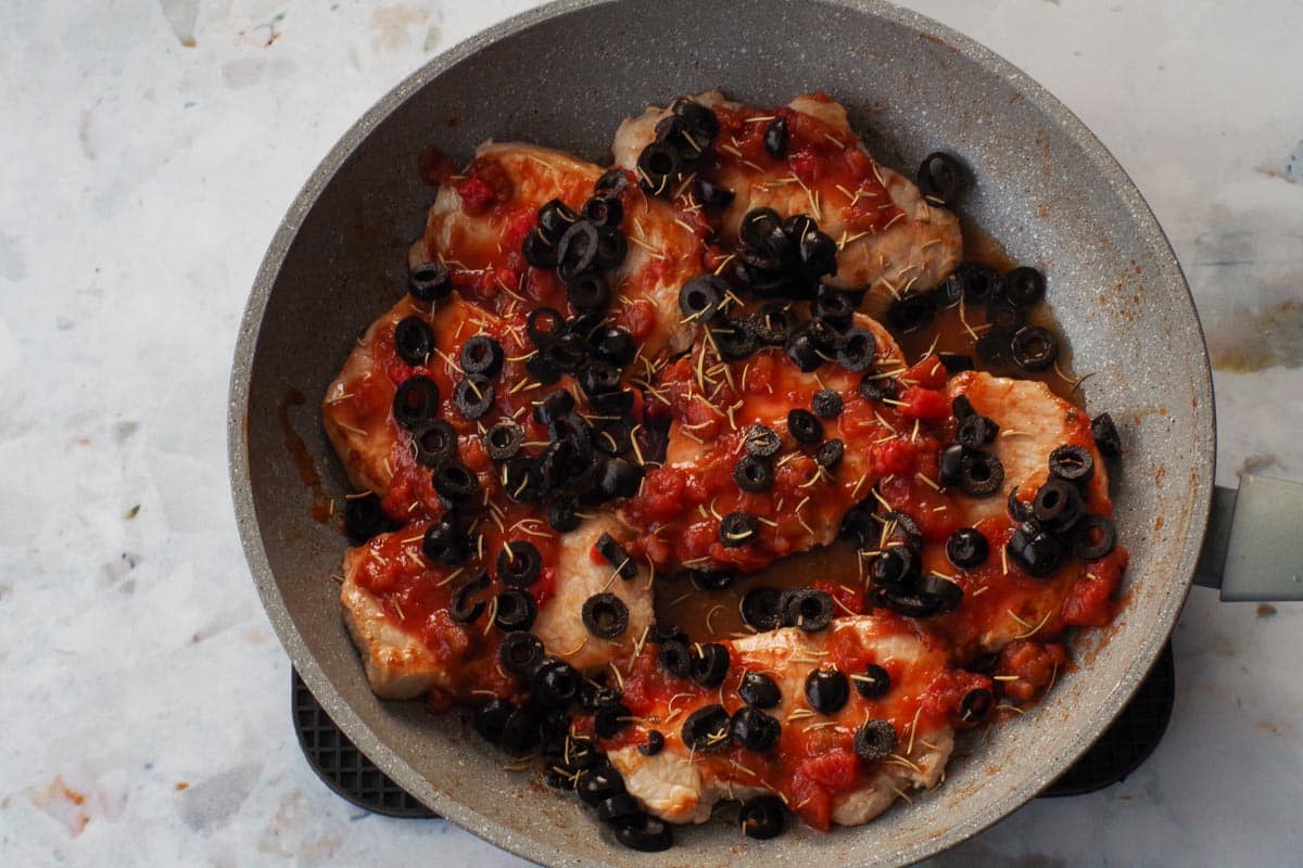 Salsa , rosemary and black olives added to browned prok in a frying pan.
