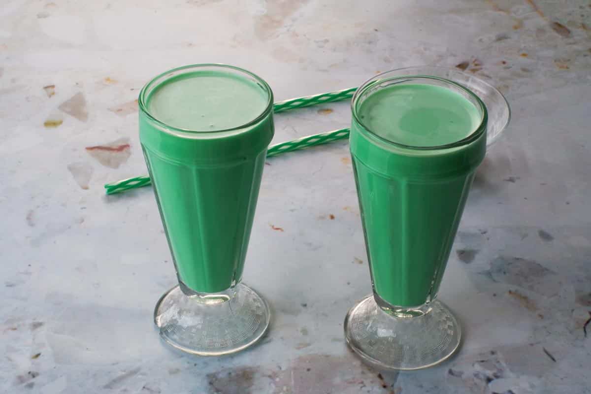 2 Milkshake glasses filled with Green Grasshopper Mocktail and 2 green straws in the background.