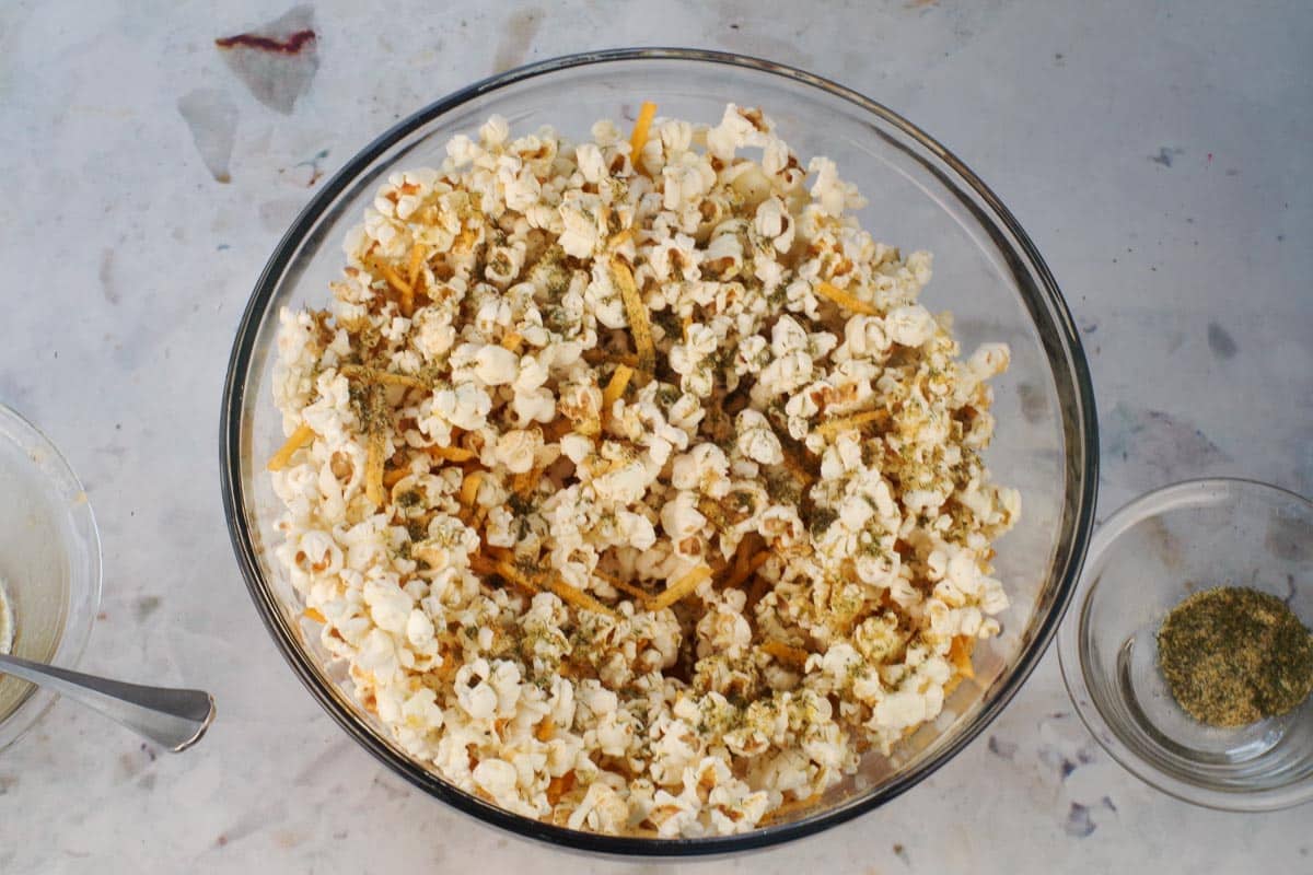 Popcorn in a large glass bowl with half the butter mixture and half the spice mixture poured on.