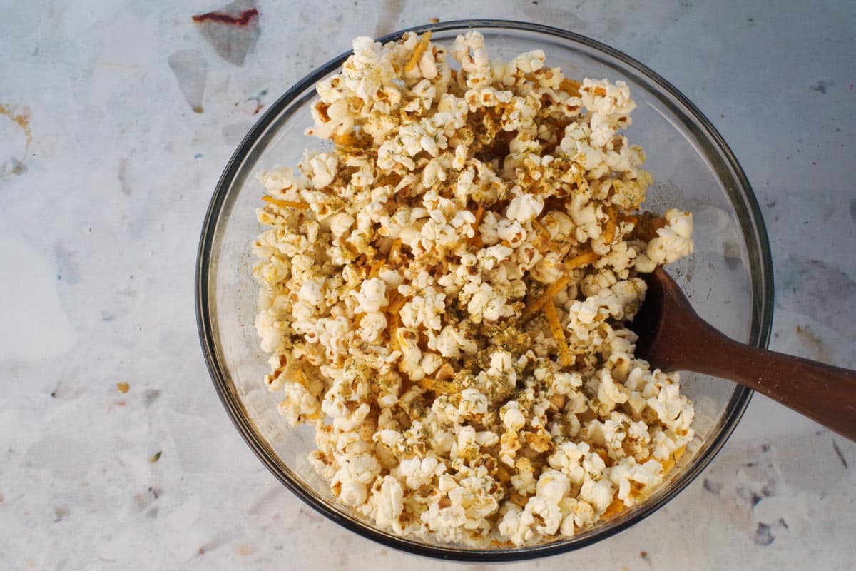 Popcorn in a large glass bowl with wooden spoon .