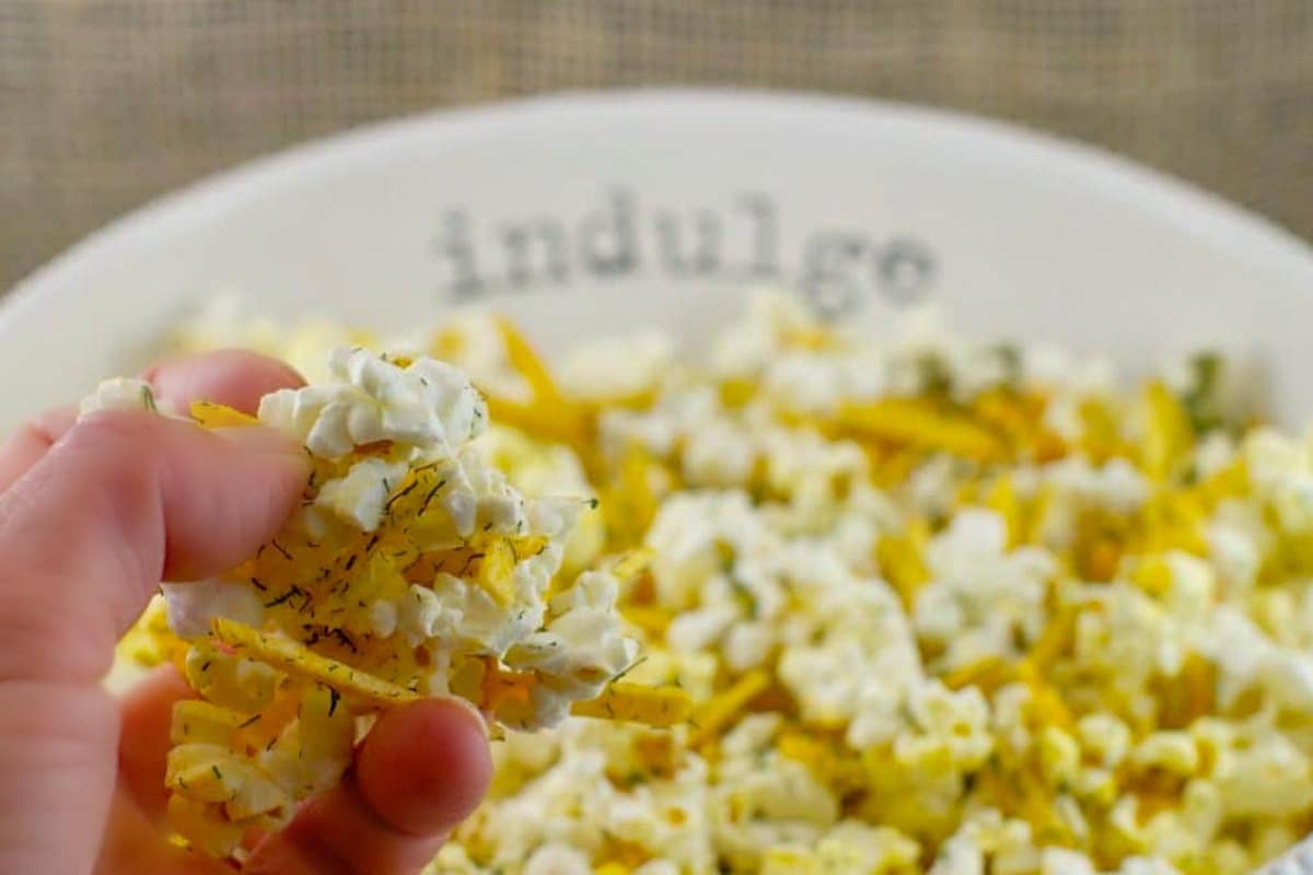 Savory popcorn in a white bowl, with the words 'indulge' on it, on faux wooden surface.