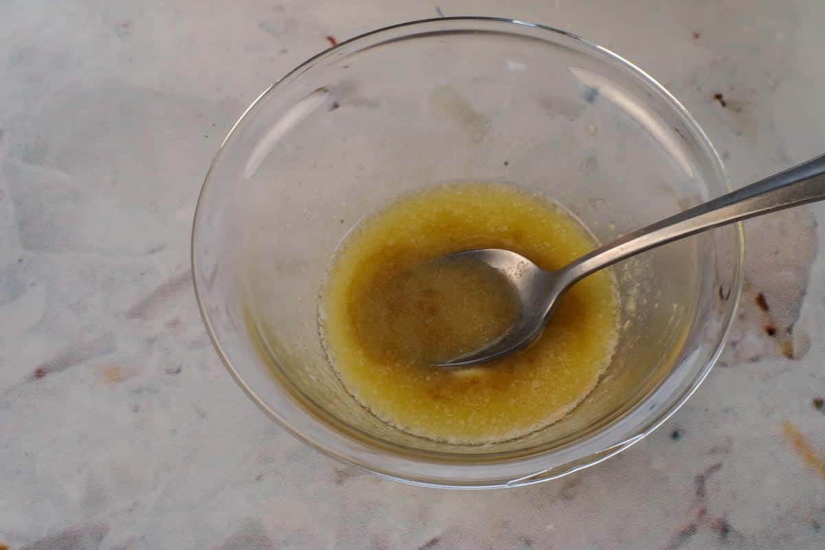 Melted butter mixed with Worcestershire sauce in a small glass bowl with a spoon.