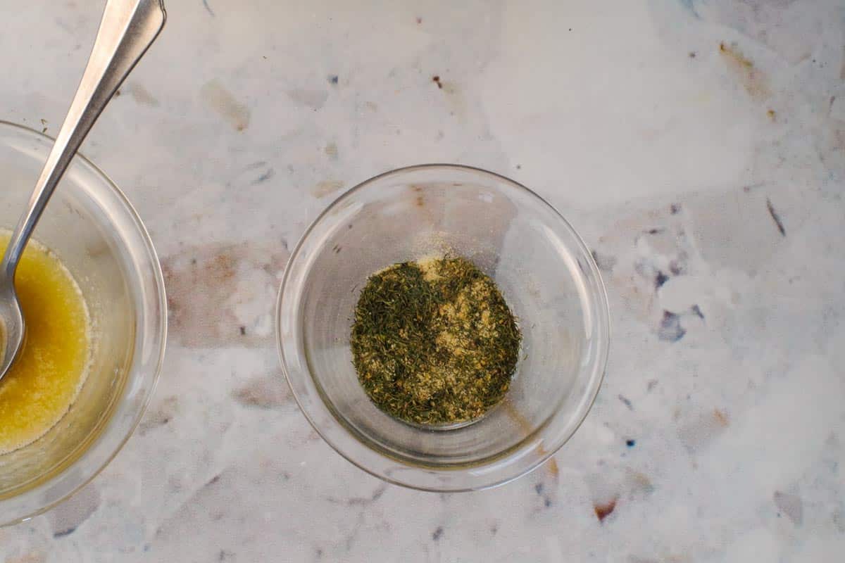 Dill, garlic powder, onion powder and lemon pepper mixed together in small glass bowl.