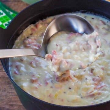 Reuben chowder in a black pot with ladle and clover leaf green and white napkins in the back