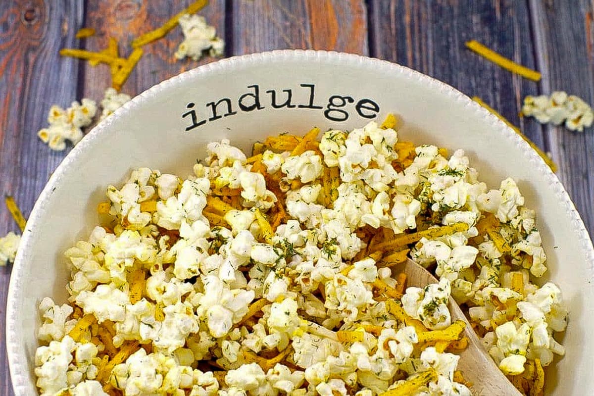 Savory popcorn in a white bowl, with the words 'indulge' on it, on faux wooden surface.