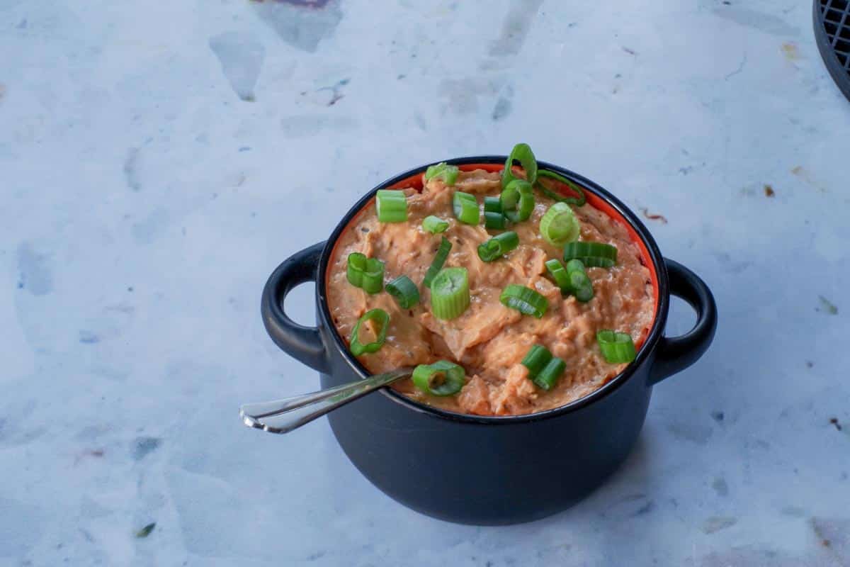 ww buffalo chicken dip in a black bowl wiht a spoon, garnished with green onion