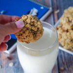 School Day cereal cookies being held over glass of milk with plate of cookies, milk and school binder in background