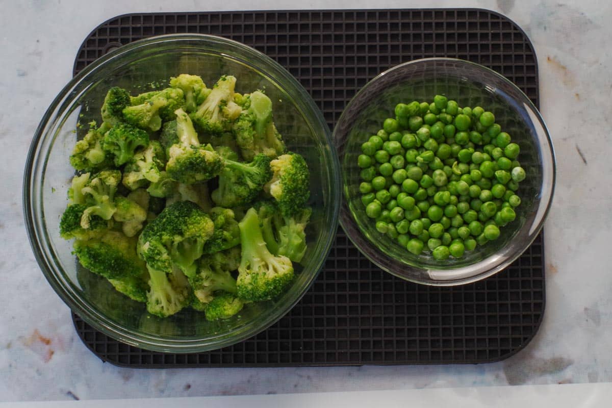 Cooked frozen brocooli and peas in glass bowls.