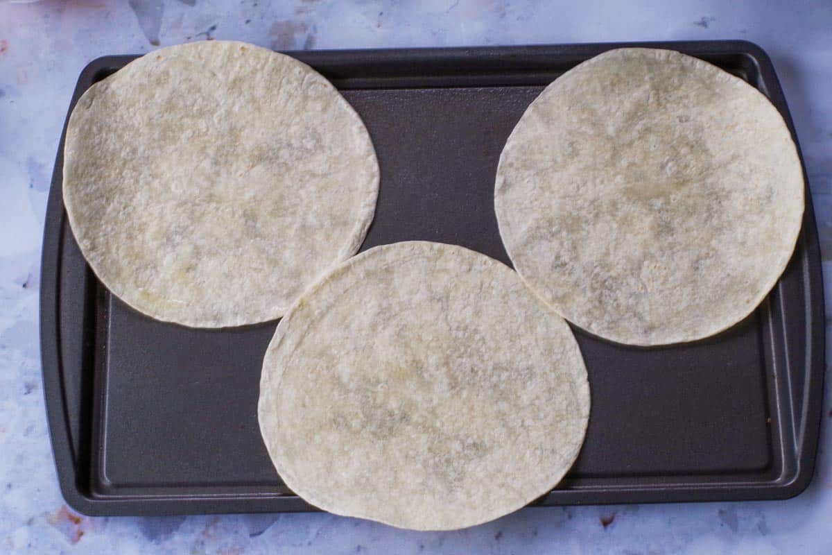 3 uncooked tortillas on a prepared baking sheet.