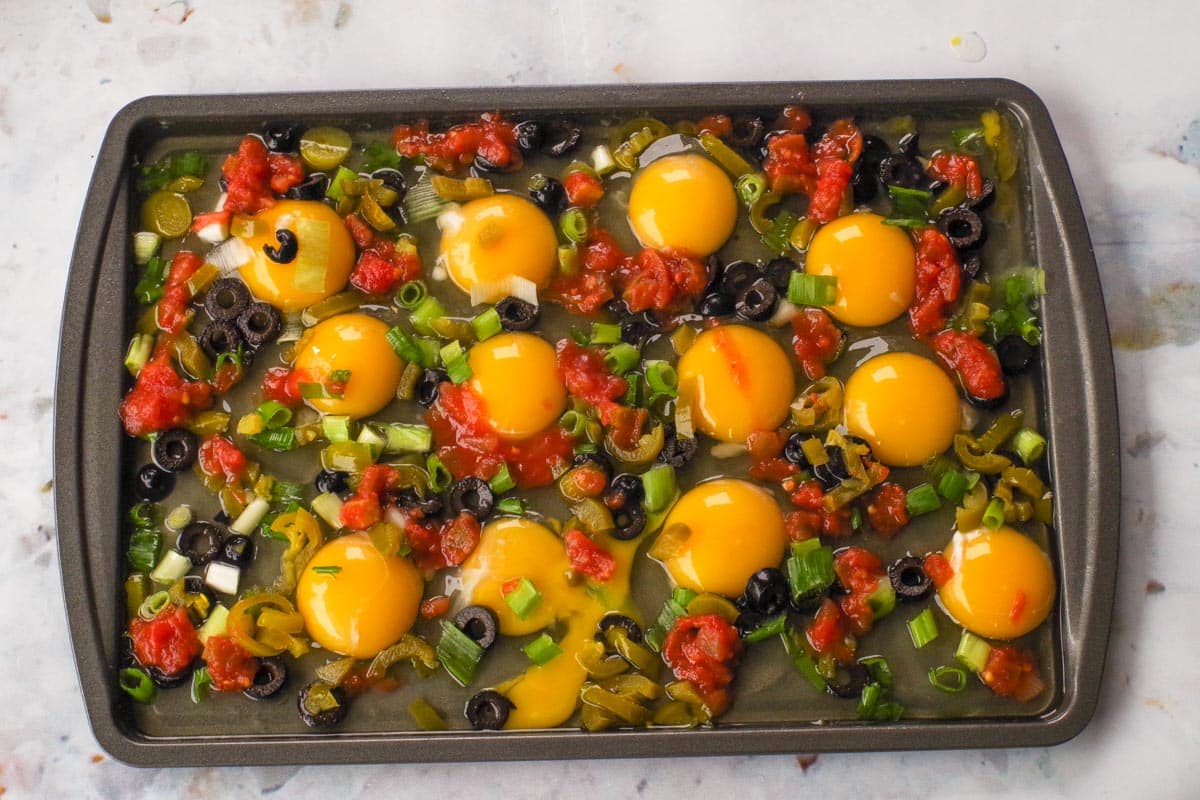 Toppings added onto sheet pan with eggs.