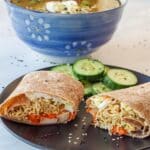 Ramen wrap on a black plate with cucumbers and ramen soup in the background