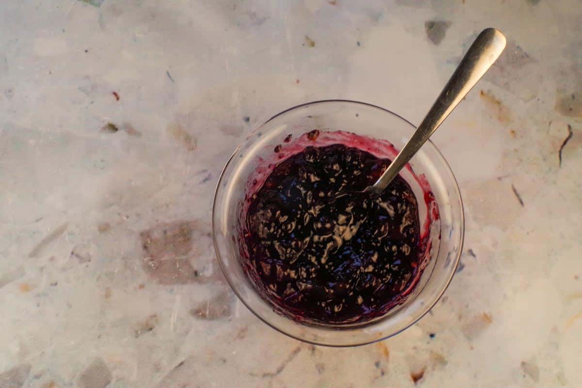 Jam and red chili sauce mixed together in a glass bowl with a spoon.