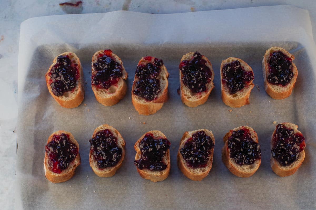 Baguette pieces with jam on parchment lined baking sheet.