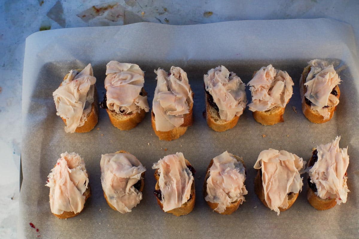 Turkey placed on top of jam covered baguette pieces.