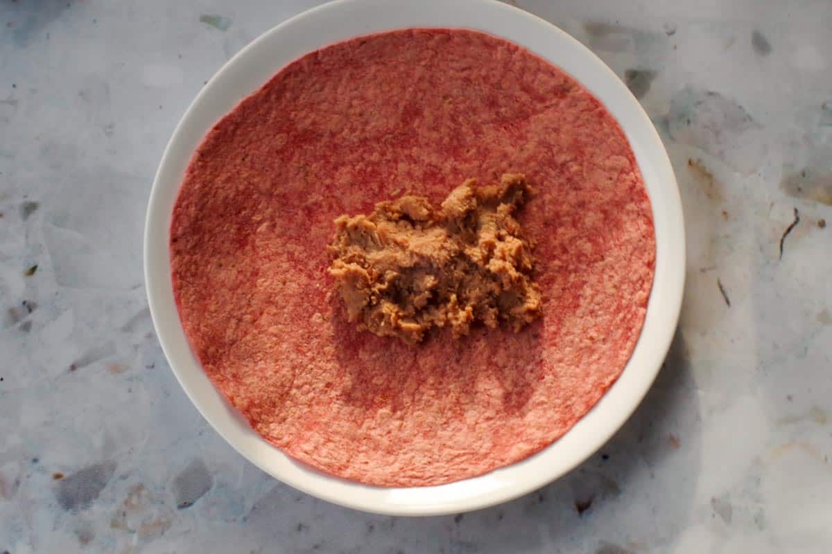 Refried beans added to middle of sun-dried tomato tortilla