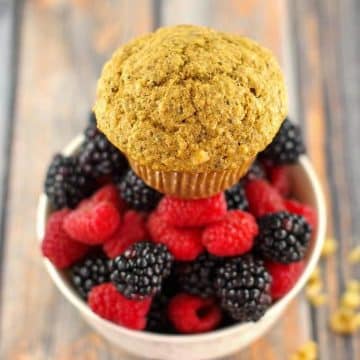 A Wheat Bran Muffins sitting on top of a bowl of fresh mixed berries, with walnuts scattered beside the bowl.