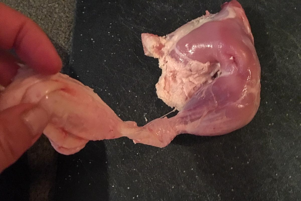 Skin being pulled off a chicken quarter piece.