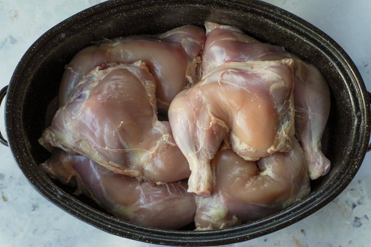 Raw chicken quarter pieces placed in roasting pan,