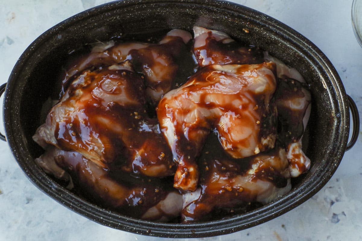 Sauce poured over raw chicken pieces in roastign pan.