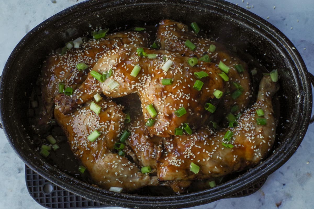 Cooked Hoisin chicken quarters garnished with sesame seeds and green onions in a roasting pan,